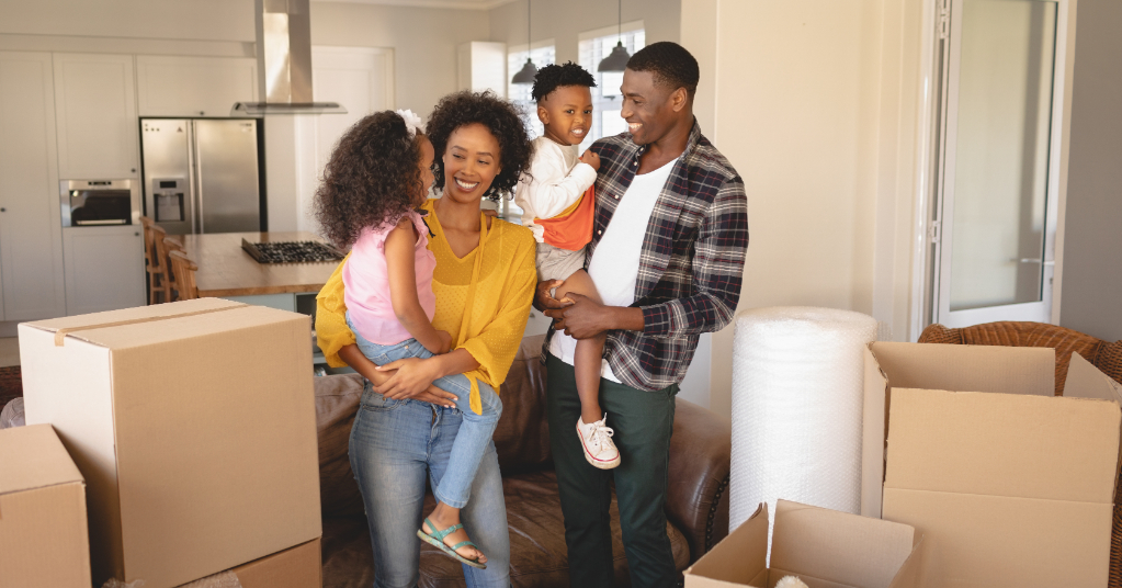 Front view of happy African American parents with their children and boxes moving in new house